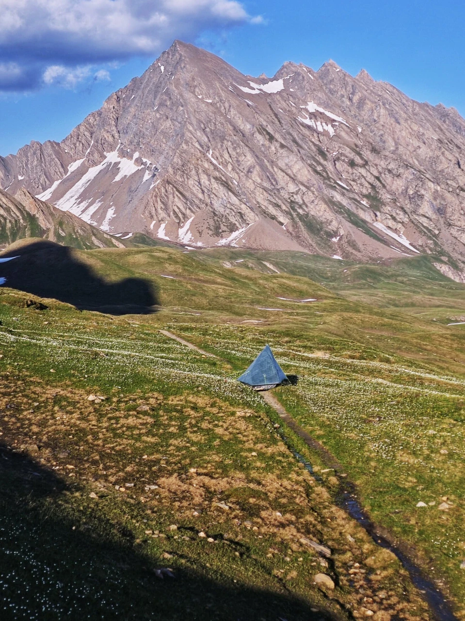 A tent pitched on a TMB pasture in early June, tiny beneath the summit with snow still lingering: an atmosphere that no longer exists once high season is under way